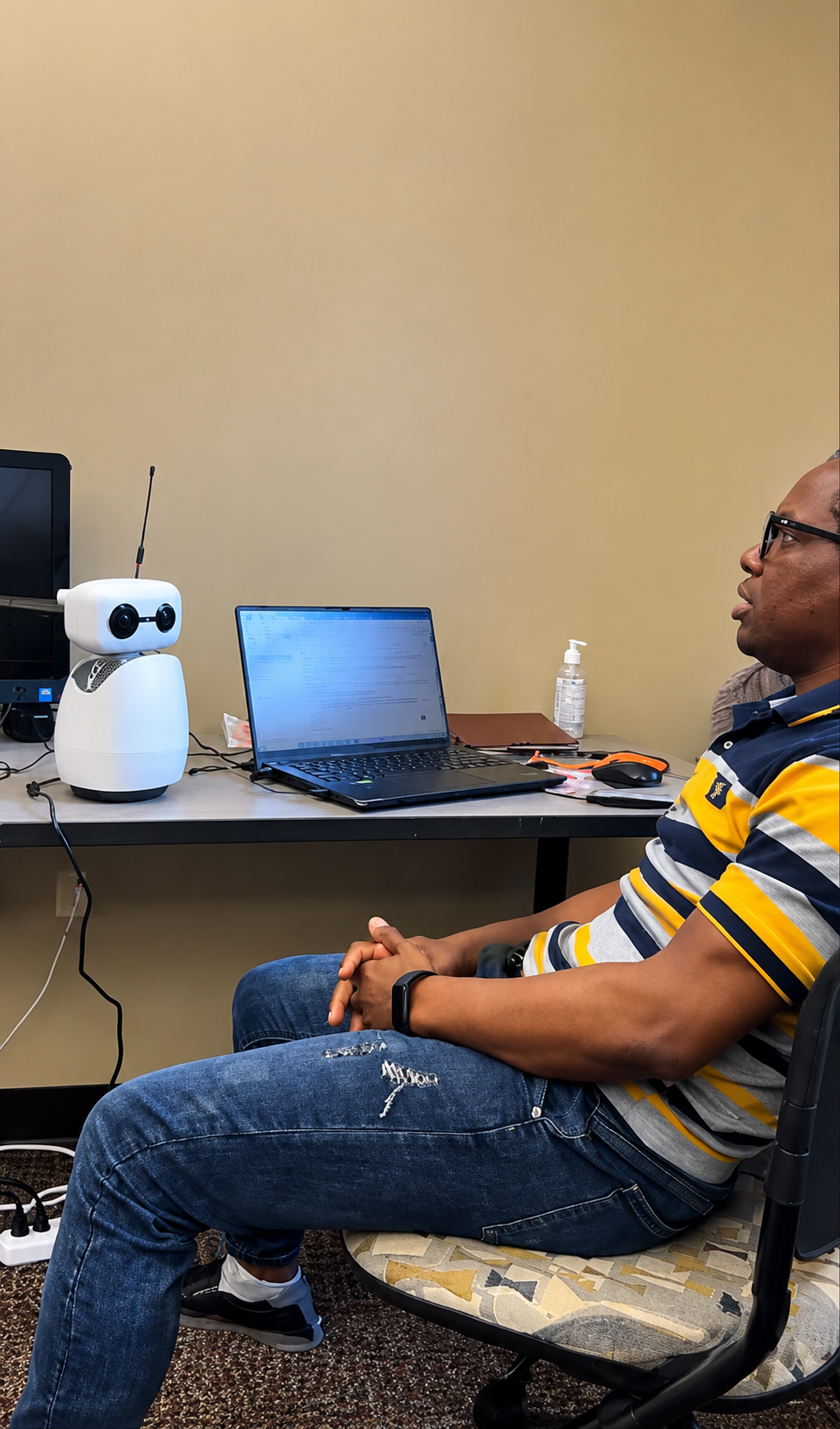 David Awoyemi working at a desk beside a Reachy Mini desktop robot connected to a laptop